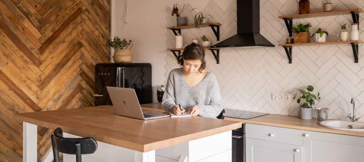 woman taking notes in kitchen with laptop