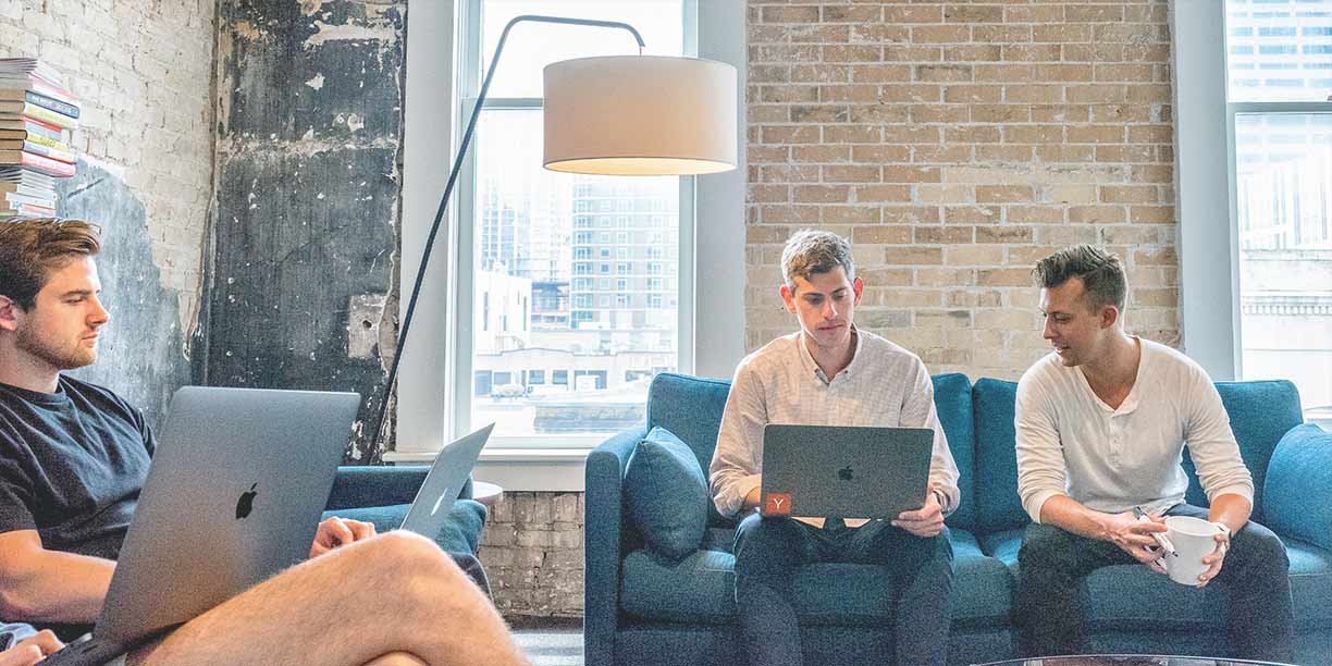 Men sitting on a blue couch working on a laptop