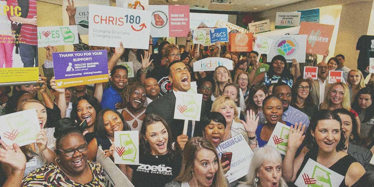 group of nonprofit volunteers in a large group holding up signs and celebrating the success of their event