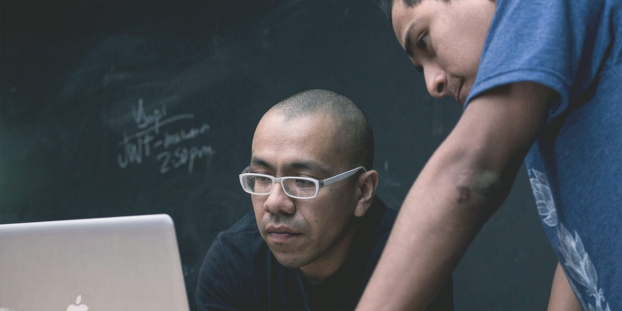 Man in black with glasses working on his nonprofit's moves management process on laptop with co-worker