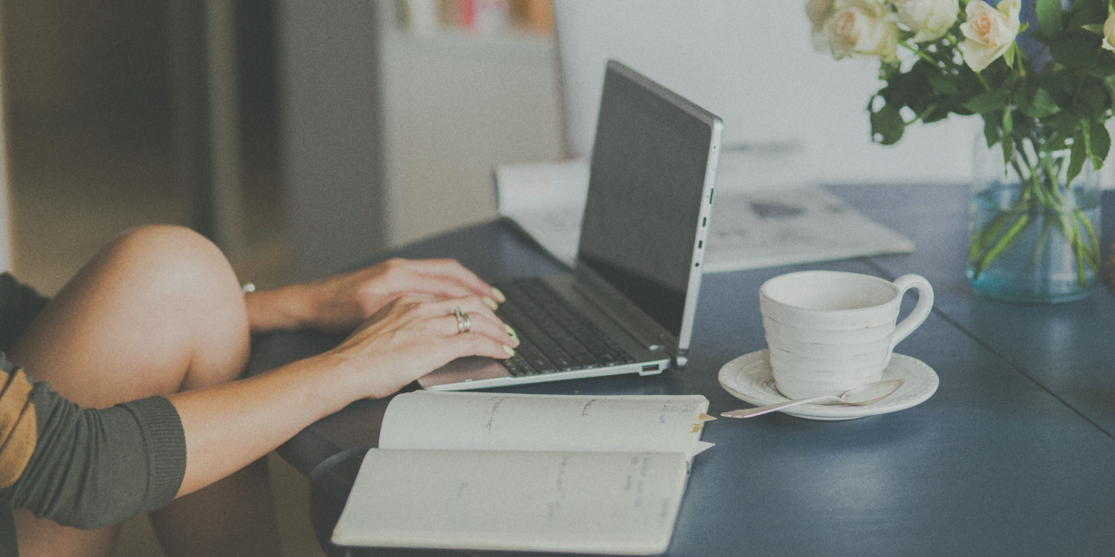 person typing on laptop with open notebook on the table