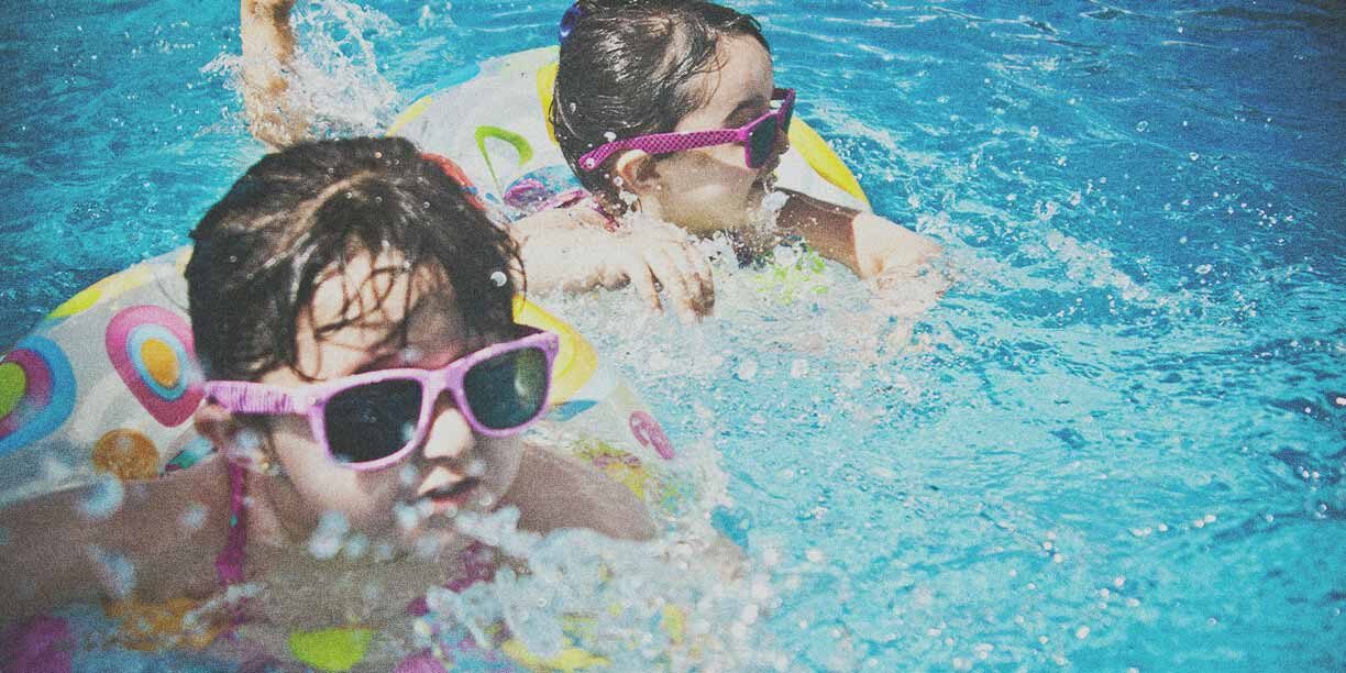 Two little girls swimming in the pool with sunglasses on
