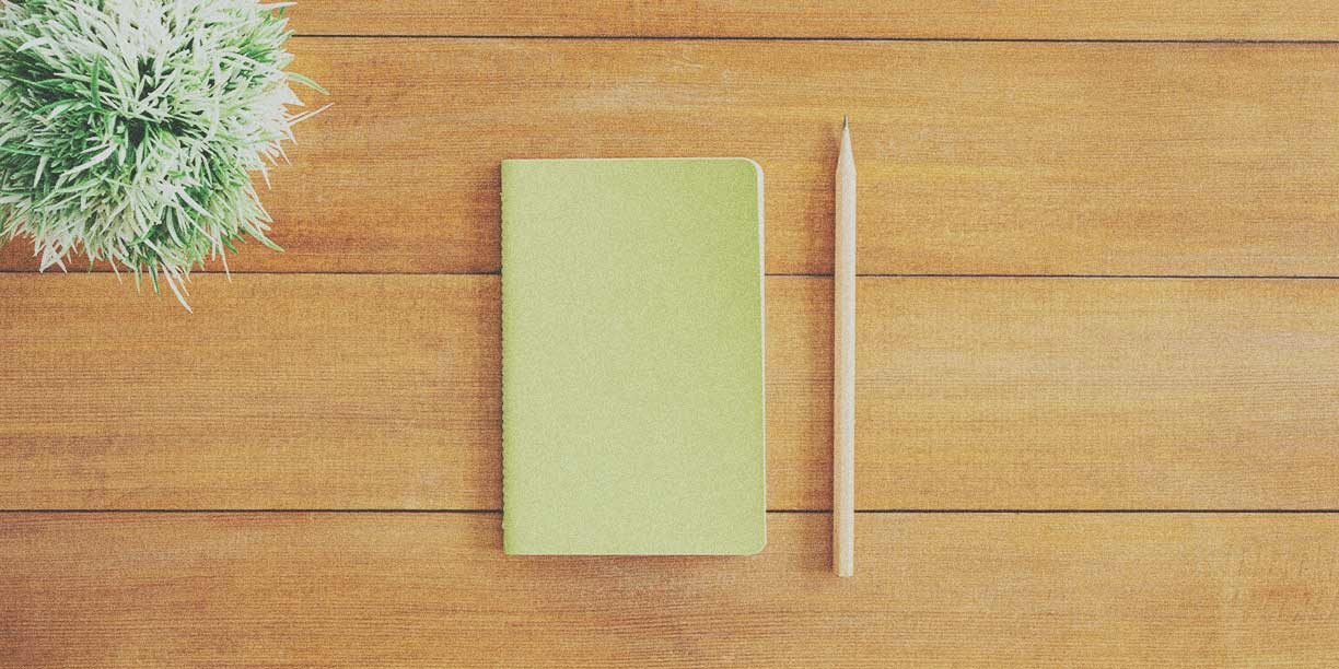 Green notebook and pencil on a brown wood desk