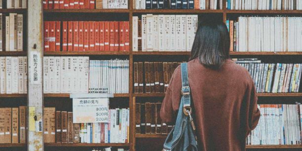 Woman in brown sweater looking at a book shelf in library