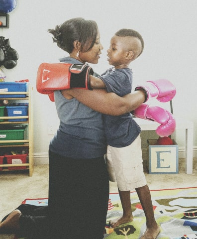 Photo of a woman and her son hugging in a playroom wearing boxing gloves