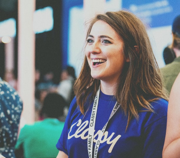 Photo of smiling young woman in a blue Classy tshirt with blurred crowd in the background