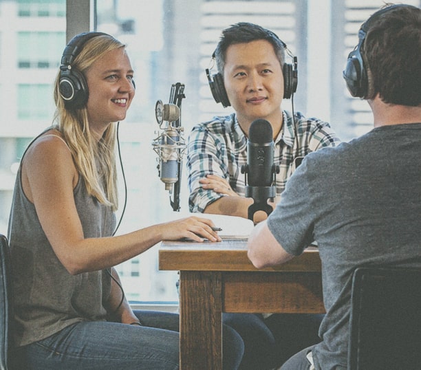 Photo of three people podcasting at a wooden table with microphones and headsets