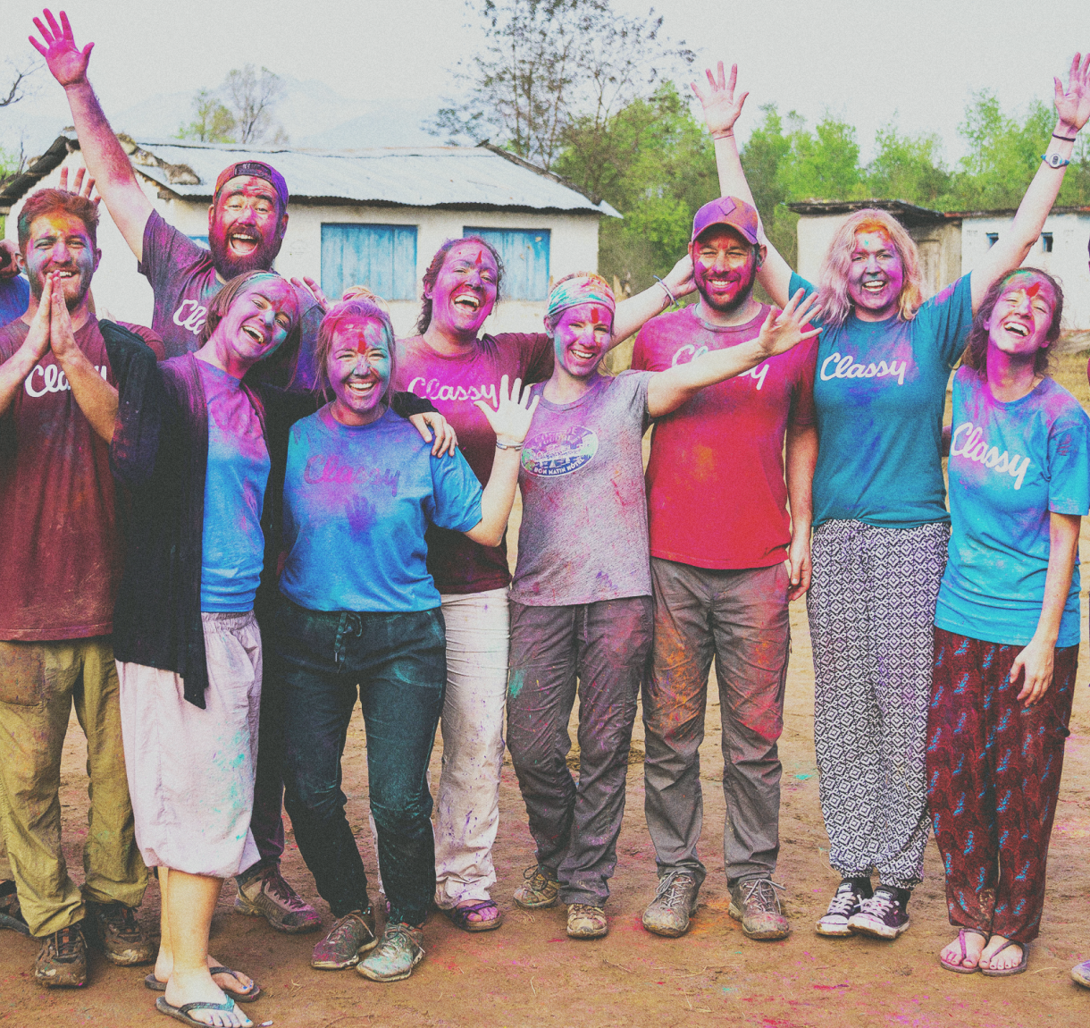 Group photo of young adults smiling outside in a dirst field covered with colorful dust