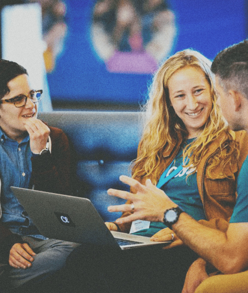 Photo of a woman sitting on a couch with a laptop smiling and engaging with the two men beside her