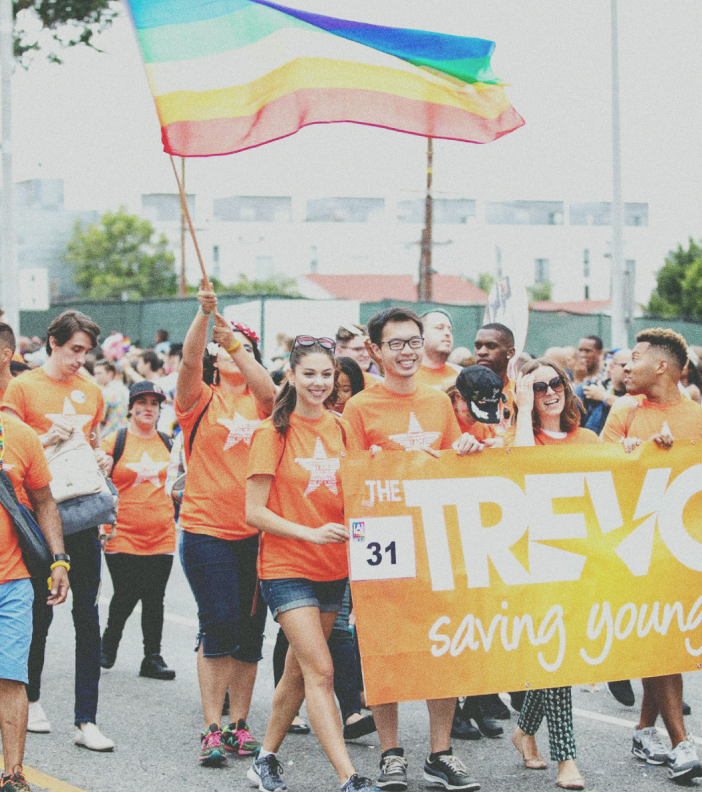 Photo of young men and women walking in a parade holding a banner and rainbow flag