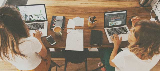 two women working at desk on laptops