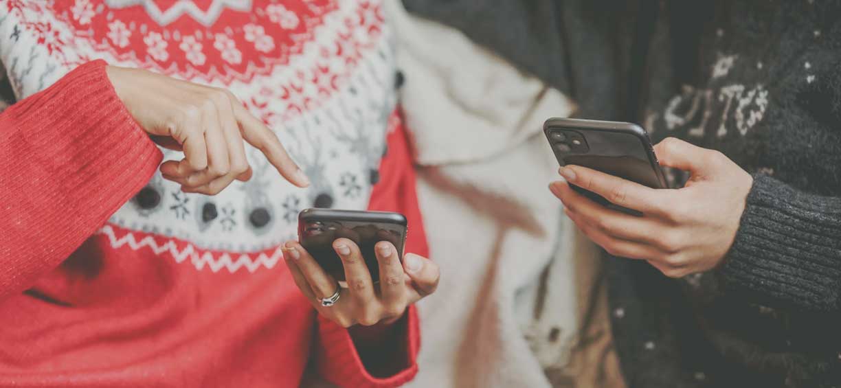 two people in holiday sweaters holding cell phones