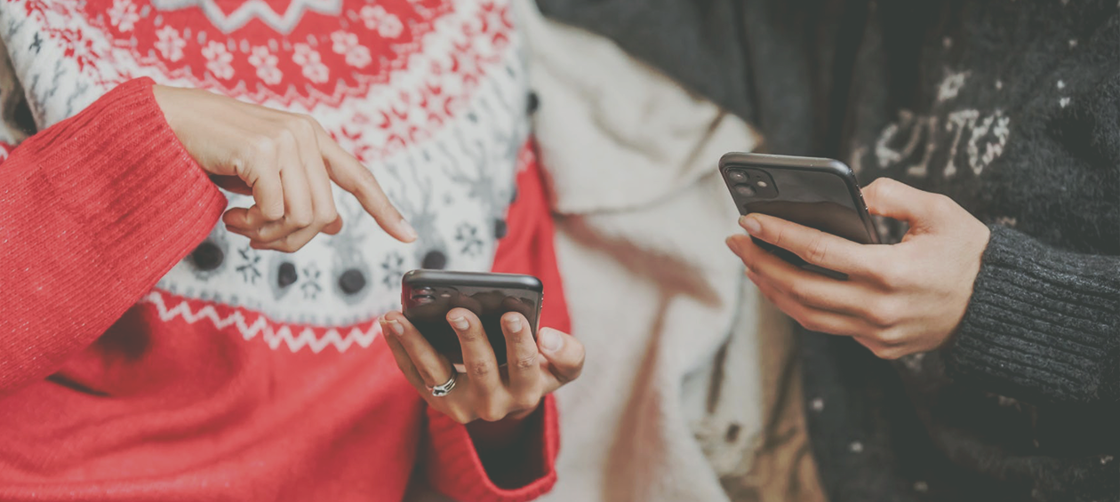 two people in holiday sweaters holding cell phones