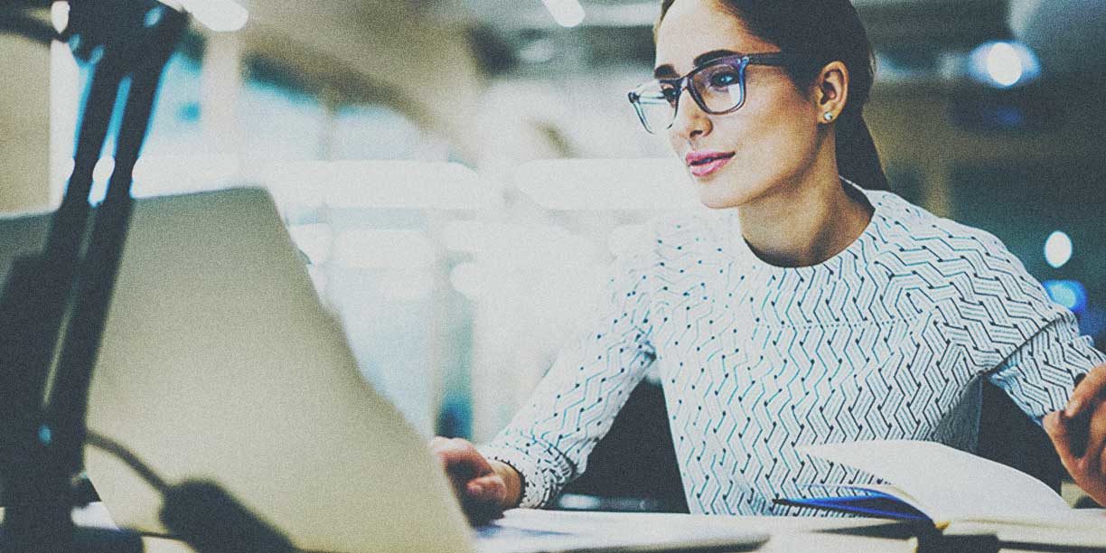 Woman in light sweater with glasses typing on computer