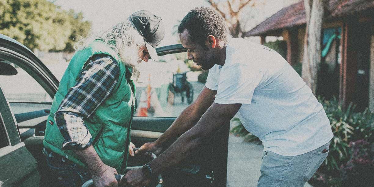 Young man in white helping elderly man in a green vest get out of car