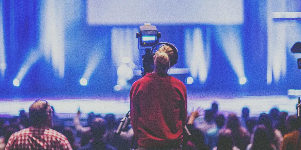 Woman in red filming a performance on stage with a large video camera