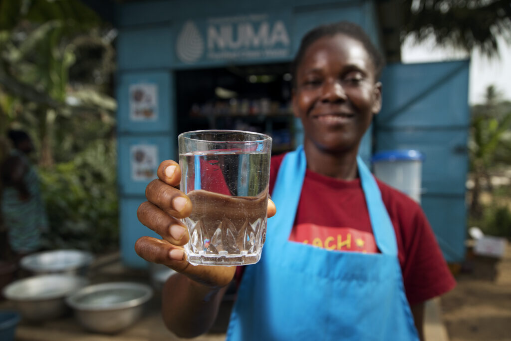 Woman in blue apron and red shirt holding up a glass of clean drinking water