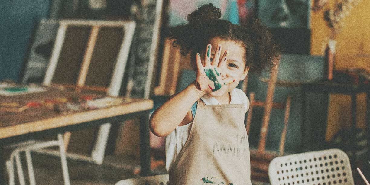 young girl in a brown apron finger painting with green paint