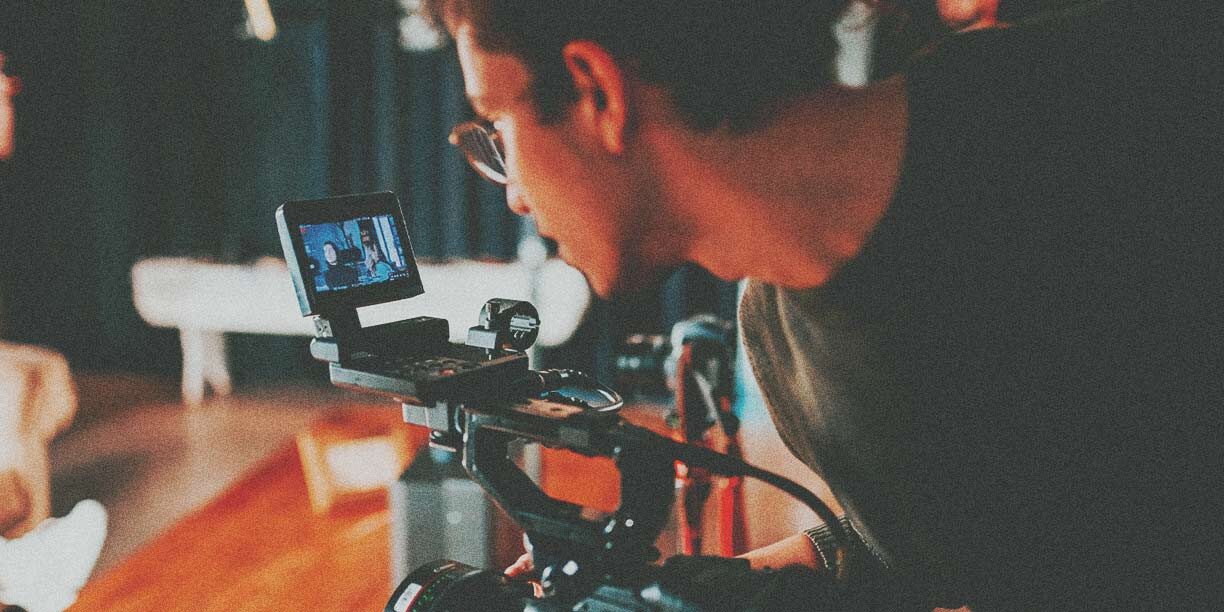 man in black tshirt and glasses filming with a video camera