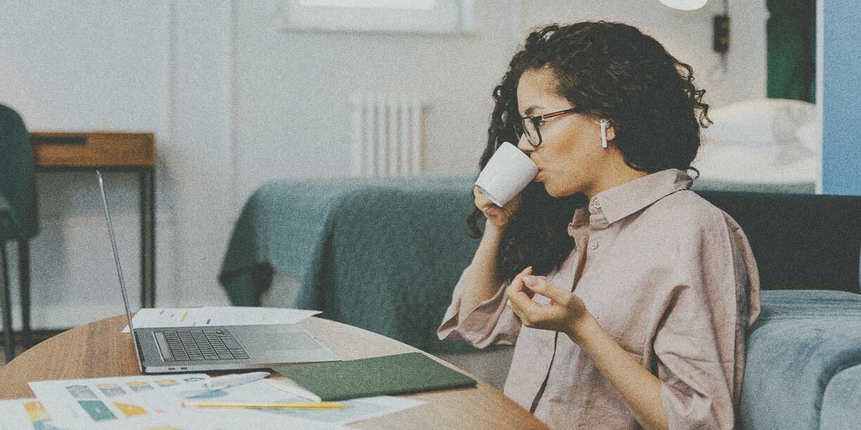 Woman in neutral color shirt sipping coffee and working on her computer