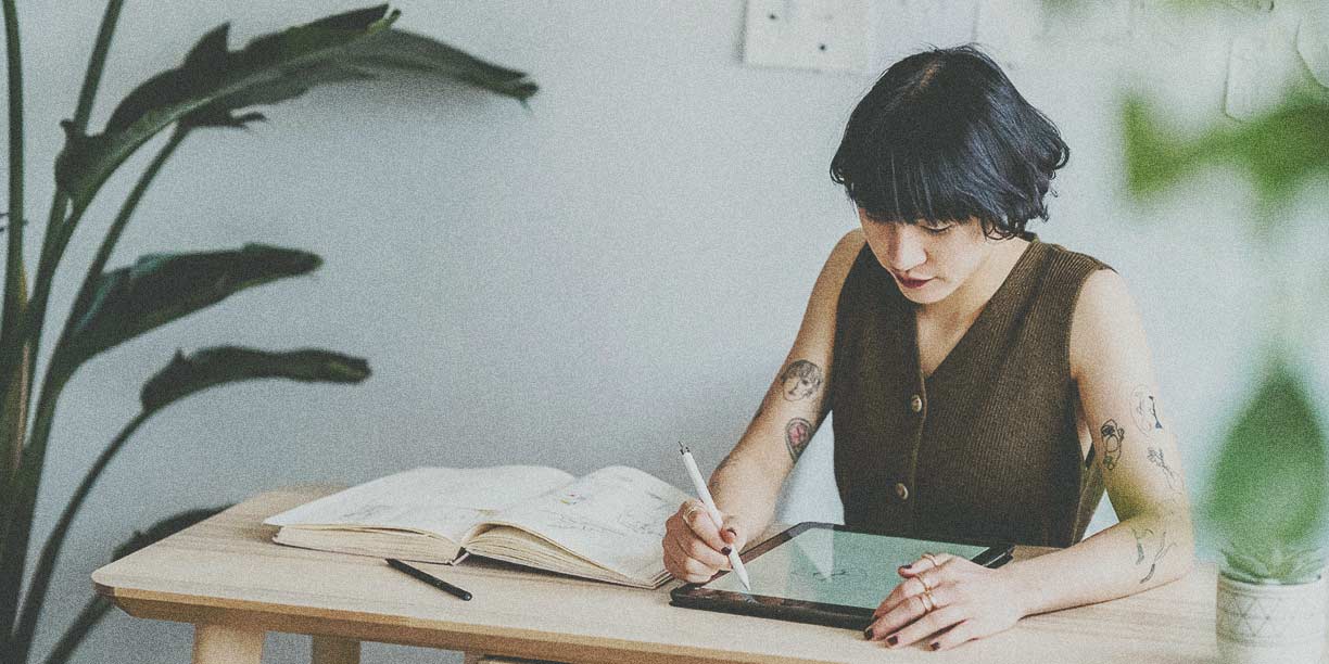 Woman in brown working at a desk, drawing on a digital tablet