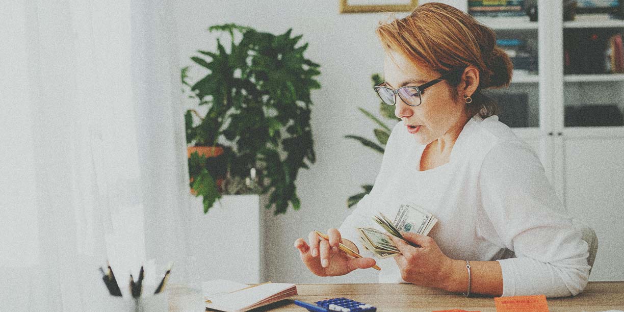 Woman in white using a calculator at her desk to count money