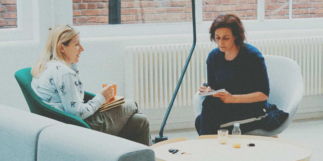 Two women sitting in chairs at office writing in notepads