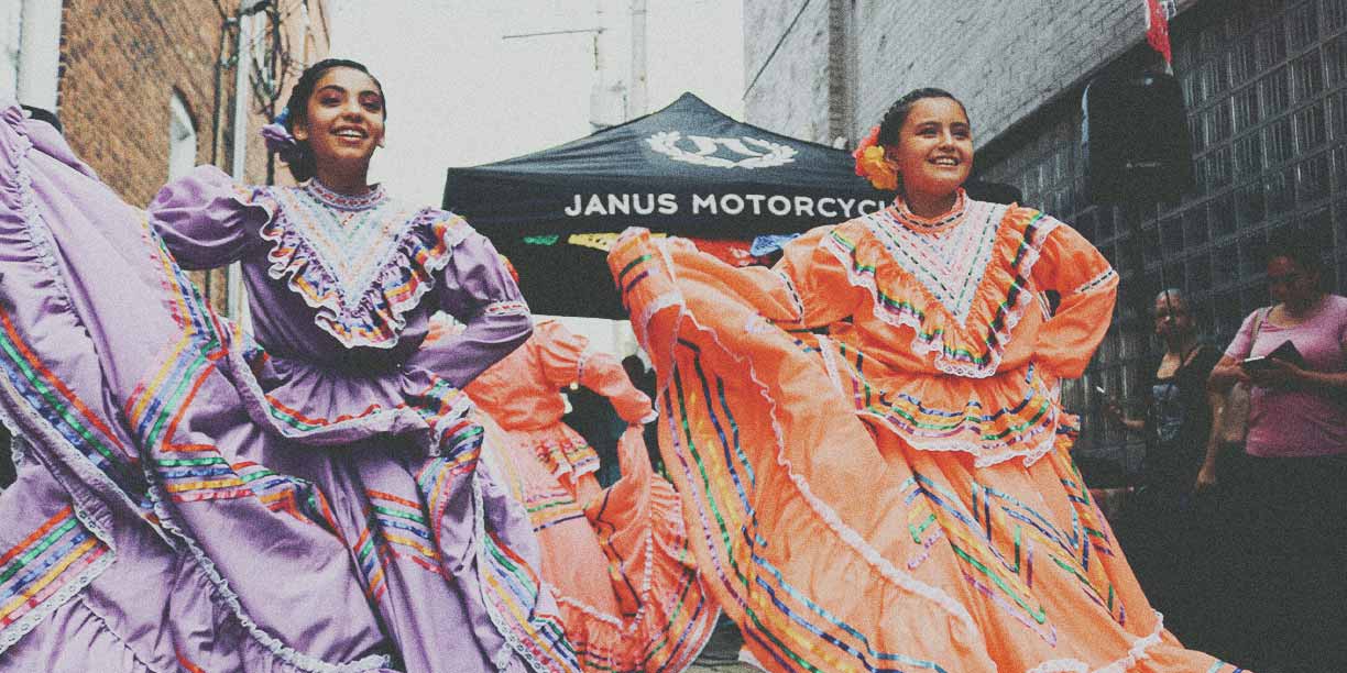 Two young women in orange and purple Hispanic dresses dancing outside