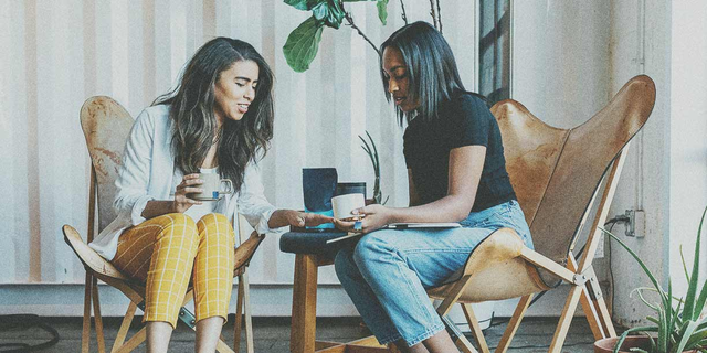 Two women sitting in brown chairs talking to each other