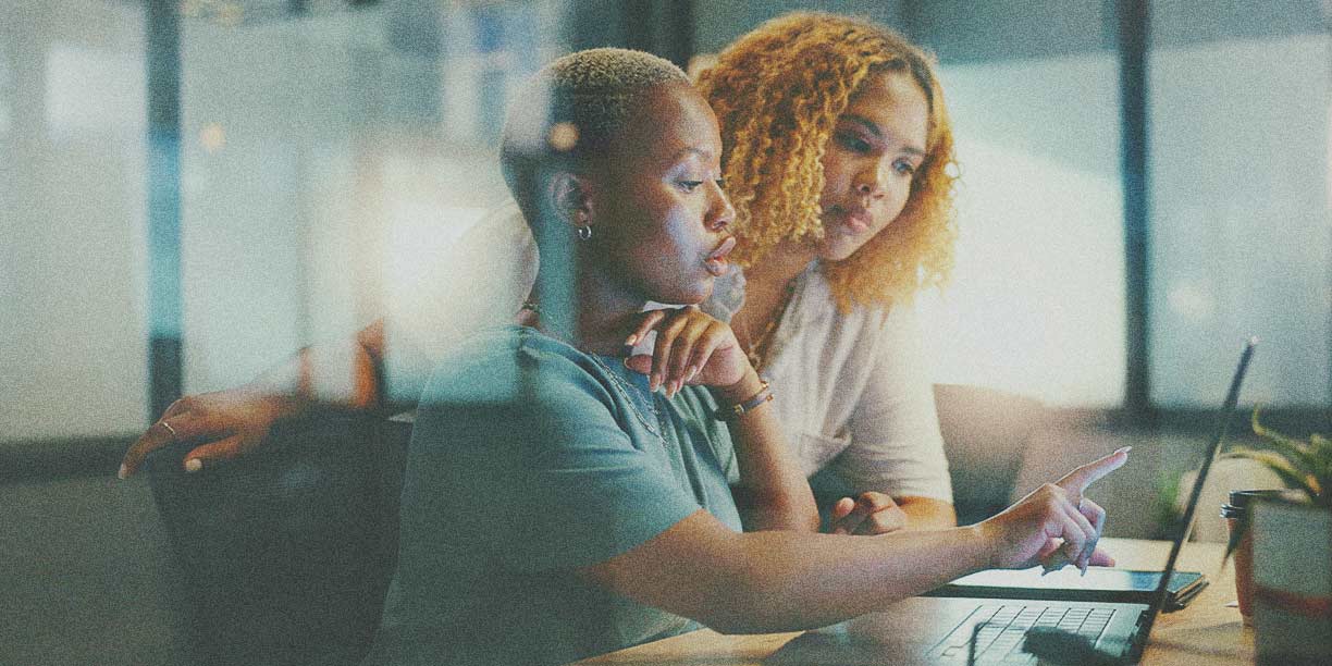 Woman in green pointing out something on her computer screen to female co-worker