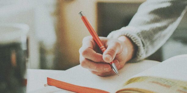 Person holding a red pen, writing in a notebook