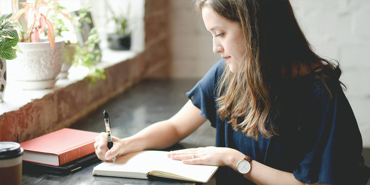 Woman in dark shirt sitting at a counter writing in a notebook