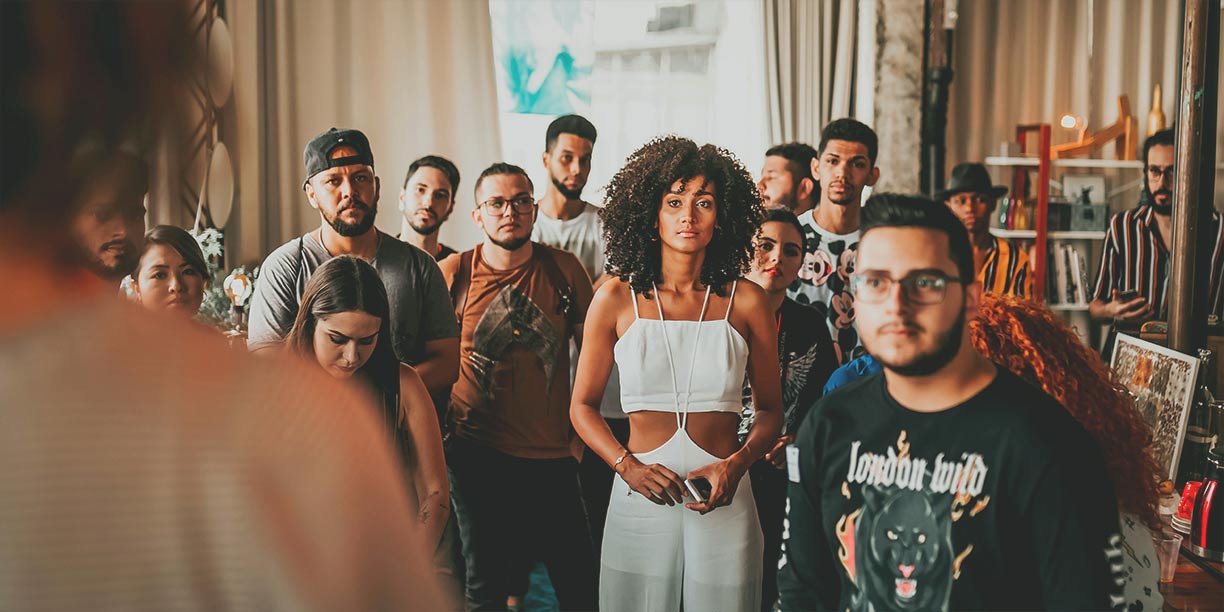 People standing in a group watching and listening to someone speak to them