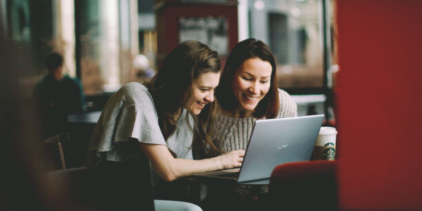 Two women working on a single laptop in a coffee shop